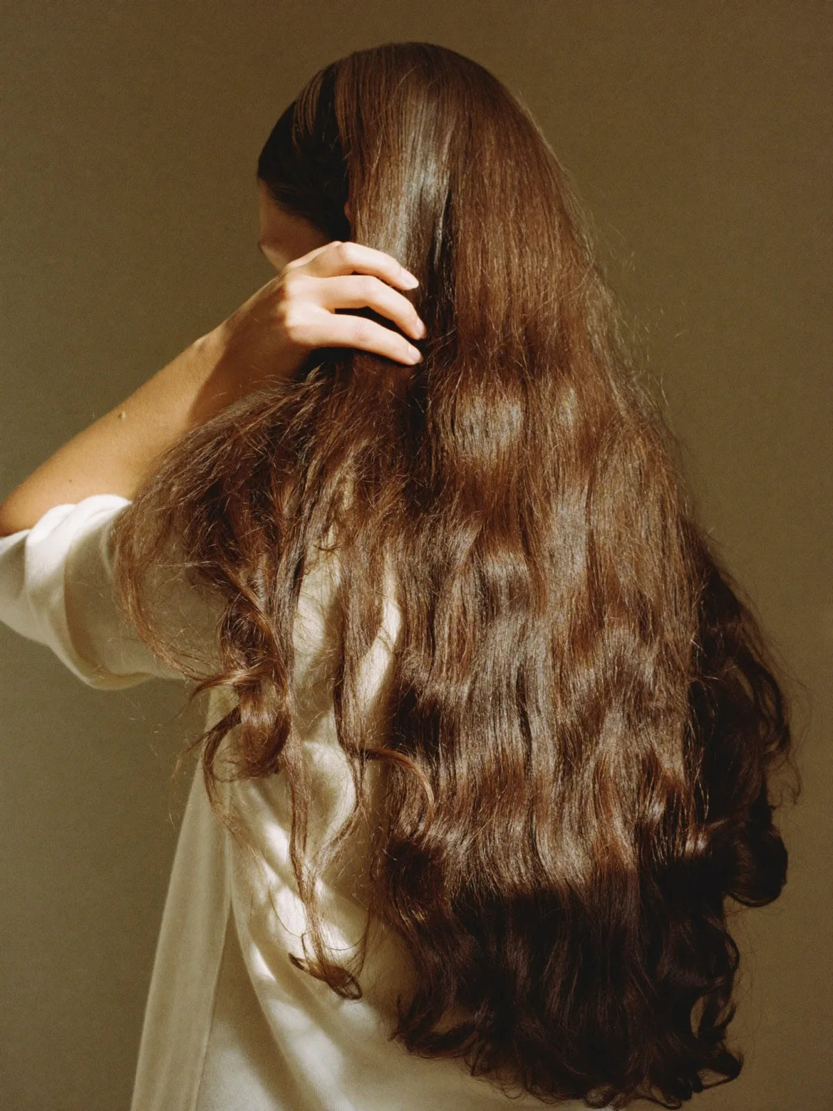 A hand resting in long brown hair in soft natural light