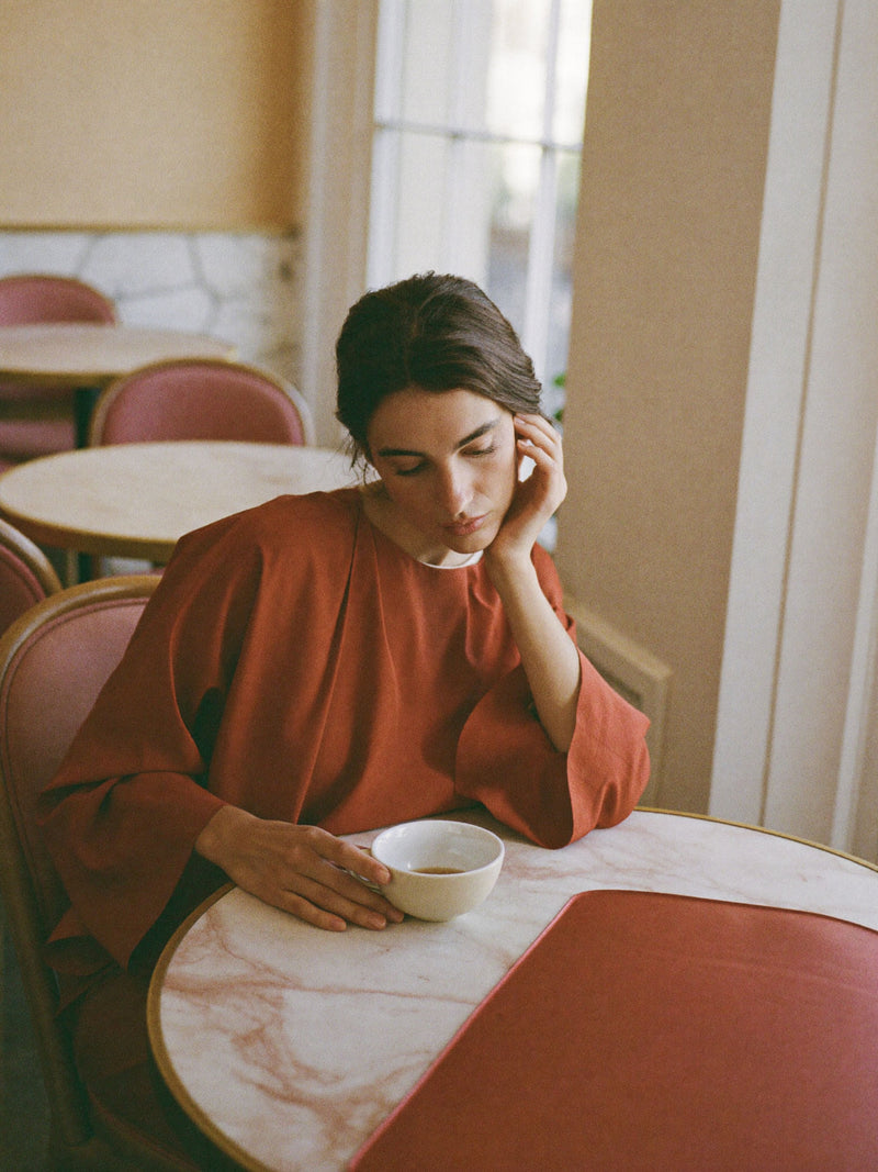 A woman pausing over tea at a marble café table during the afternoon