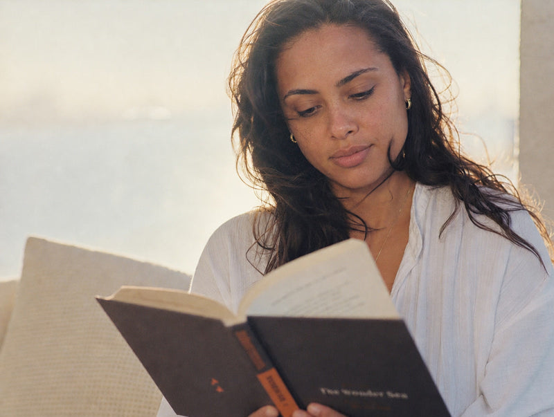 A woman absorbed in a book in soft coastal light